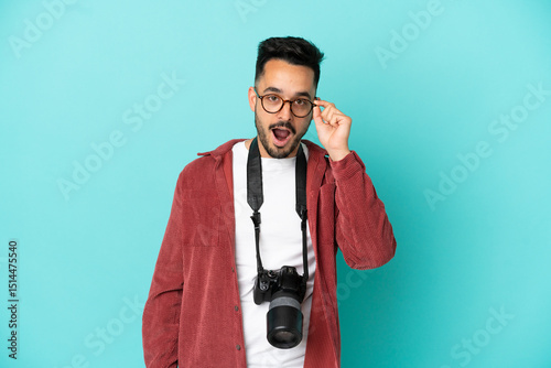 Young photographer caucasian man isolated on blue background with glasses and surprised photo
