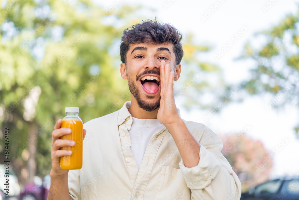Fototapeta premium Young Arabian handsome man holding an orange juice at outdoors shouting with mouth wide open