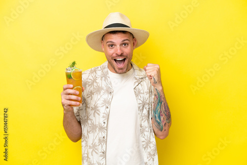 Young caucasian man holding a cocktail isolated on yellow background celebrating a victory in winner position