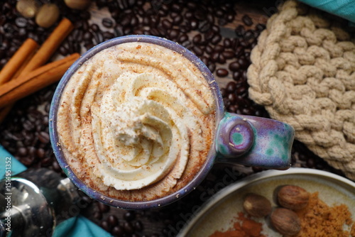 Cup or mug of coffee in a blue ceramic cup with whipped cream and a dash of nutmeg or cinnamon.  Coffee beans surrounding a cozy cup of coffee in a blue mug.  