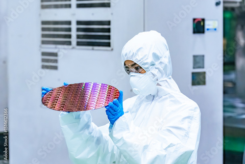 半導体工場でシリコンウエハーを検査する防護服を着た女性作業員