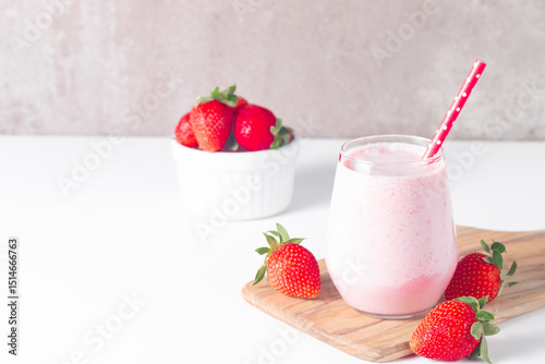 Glass of fresh strawberry milkshake, smoothie and fresh strawberries on white and wooden background. Healthy food and drink concept.
