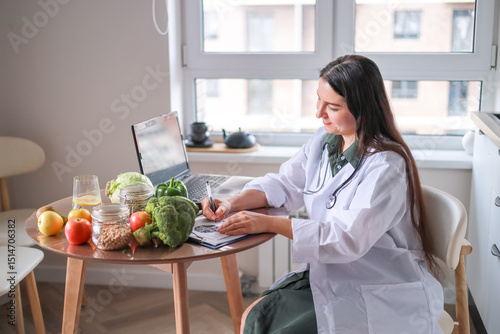 dietitian in a medical coat working with clients online at a table full of fresh vegetables and fruits using a laptop and a tablet. health concept, medical services.