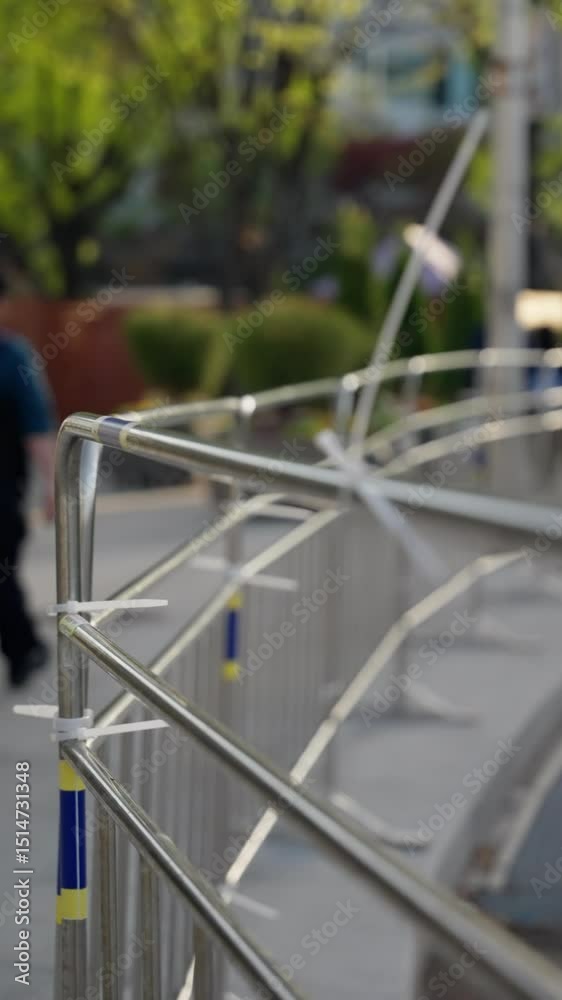 Temporary metal barricades secured with cable ties line a city sidewalk, providing controlled pedestrian access and safety measures in an urban outdoor area. Temporary metal barricades secured with cable ties line a city sidewalk, providing controlled pedestrian access and safety measures in an urban outdoor area.