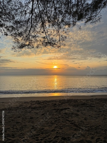 A serene scene of a golden sunset reflecting on the calm ocean surface with gentle waves lapping the shore.