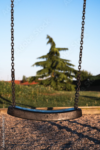 Swing set in a serene playground surrounded by greenery and trees during the golden hour of the evening