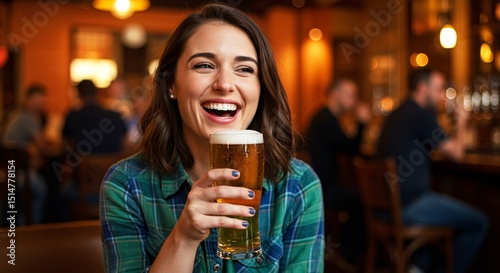 Woman laughing holding a glass of beer. She's sitting at a bar and is happy. Friends and bokeh lights in background add to atmosphere.