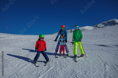 Mother teach kids to snow plow on sunlit slope with mount view