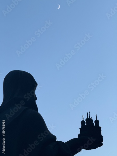 silhouette of a clergyman priest holding a model of a church in his hands against the night sky
