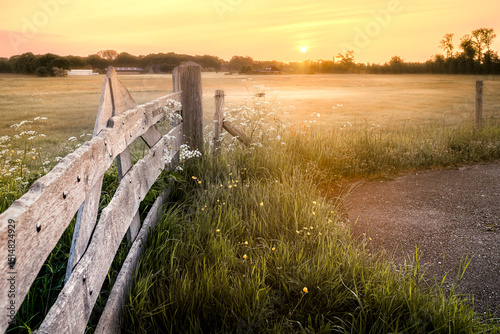 Meadows with wooden fence and rising sun in the early morning