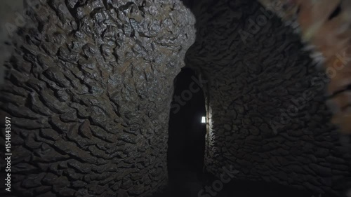 Narrow cave passage with rough stone walls dimly lit by modern lanterns along the corridor

