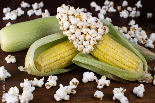a couple of corn on a wooden table with corn grains and popcorn with popcorns over around