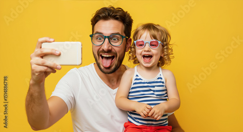 Excited father and curly child taking selfie wearing funny glasses on yellow background. Joyful family photography moment. Father's Day camera and entertainment service promotions