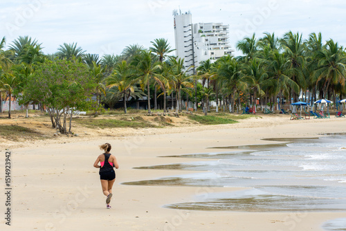 Fototapeta Naklejka Na Ścianę i Meble -  Woman enjoys running along the beach with rocks and calm water in the background during a sunny day