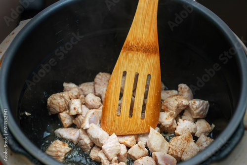 Bamboo cooking spatula stirring small pieces of frying poultry meat in a pan, showcasing healthy cooking techniques