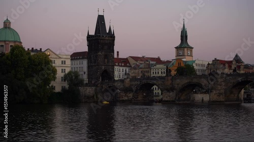 A captivating view of Prague at twilight, showcasing the historic Charles Bridge and its iconic towers reflected in the calm Vltava river. The atmospheric dusk light bathes the architectural landscape