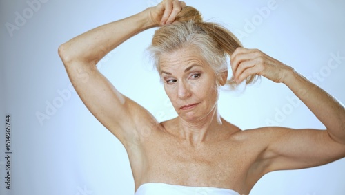 A happy mature woman smiles as she elegantly gathers her hair into a ponytail in a bright spa environment. The warm ambiance enhances her relaxed demeanor. photo