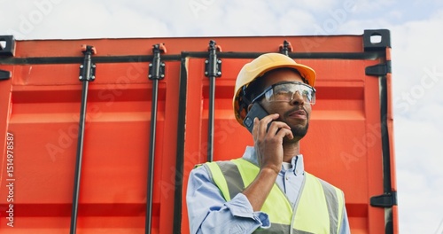 Foto Portrait of focused successful African-American worker of transportation company talking on phone wearing helmet, safety helmet
