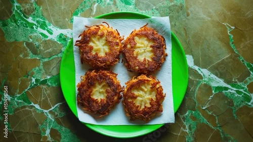 Golden Crispy Potato Latkes on a Bright Green Plate with Textured Background Showcasing a Garnish of Paper Towels for Absorbing Excess Oil photo