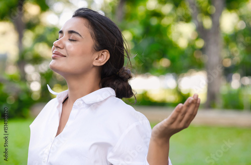 Positive relaxed happy refreshing young south asian woman taking a deep breath of clean unpolluted air in urban park, good summer, summer wellness, good sunlight exposure environment concept image