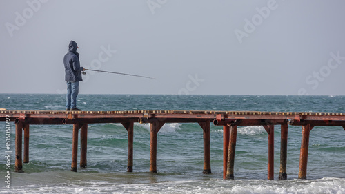 Fishing by the sea. A man standing on the pier fishing with a fishing rod. In inclement weather, people fish on the coast.