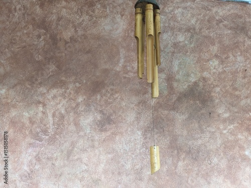 A bamboo wind chime hanging against a textured brown wall, showcasing natural materials and minimalistic outdoor decor.