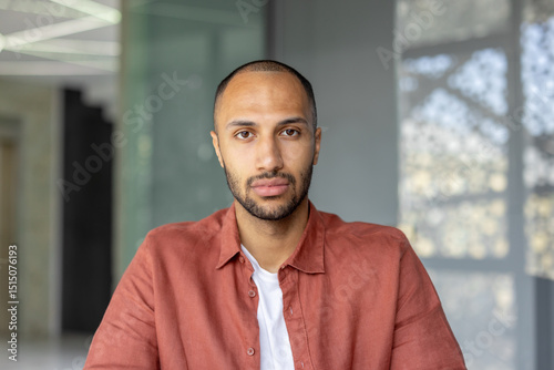 A portrait of a young man with a short haircut and a red shirt, looking directly at the camera. photo