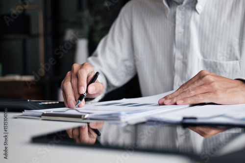 Focused businessman checking reports and verifying office documents with calculator and paper files on table