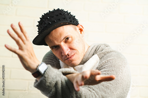 A man wearing a black cap and a gray sweater is captured in motion, dancing gracefully with fluid movements. His outfit contrasts against the background as he enjoys his dance.