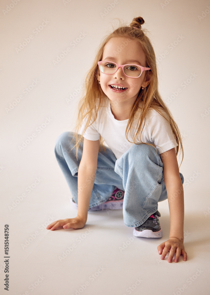 Φωτογραφία An active and cheerful young girl with long blond hair and glasses sits on her haunches and smiles
