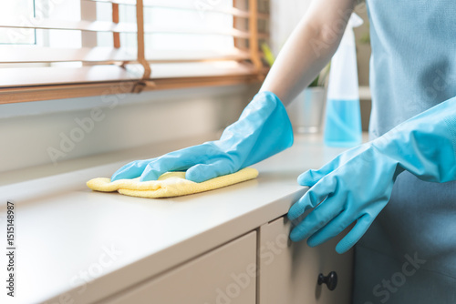 Fotografi Cleanliness household asian young woman working chore cleaning on cupboard at home, hand wearing glove and using wiping with microfiber cloth remove dust in living room