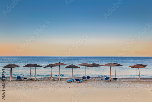 Fototapeta Naklejka Na Ścianę i Meble -  straw umbrella and sun loungers in line on a beach at sunset in Peloponnese Greece