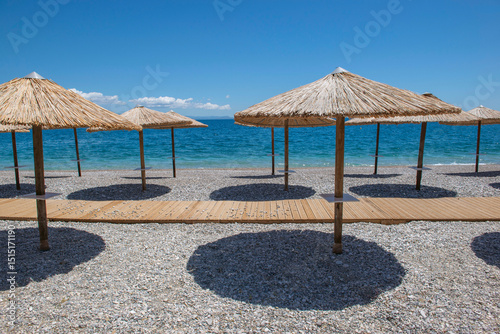 Fototapeta Naklejka Na Ścianę i Meble -  straw umbrella on a beach iof pebbles n Peloponnese, Greece with their well drawn shadow in front beautiful sea