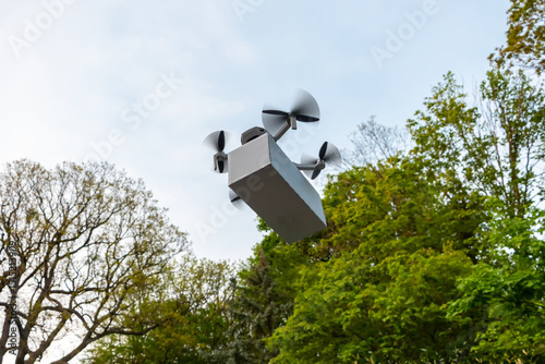 Drone with cargo on the background of green trees: modern drone with a box flies in the sky, transporting parcels in urban conditions. The concept of fast delivery and innovative technologies.