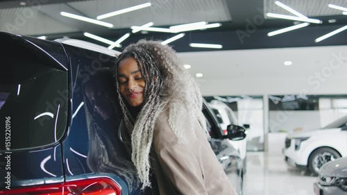 Excited woman enjoys her new car in a modern showroom filled with vibrant lights and sleek vehicles during the day