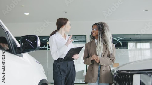 Sales consultant discussing features with a customer in a modern car dealership during daylight