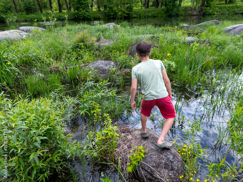 A young boy standing on a rock in the middle of a pond is preparing to bend