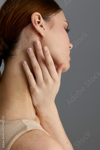 Beauty woman with smooth skin touching her neck gently, showcasing natural elegance and delicate hand pose against a soft neutral background. photo