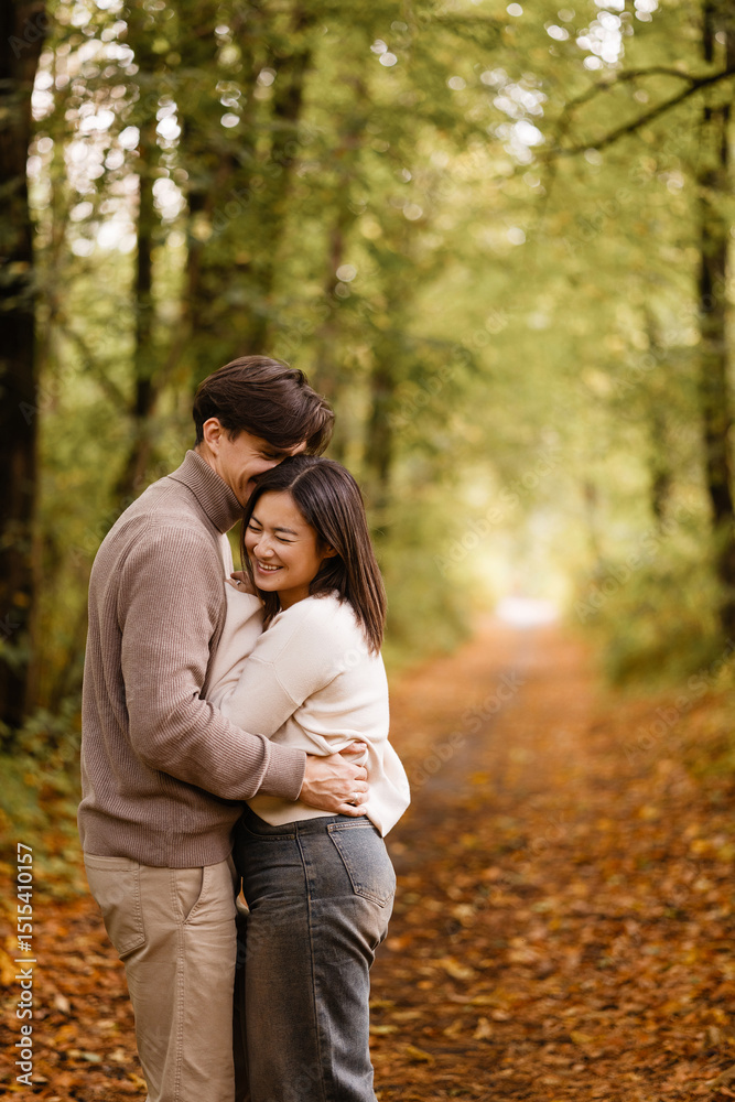 Side view of a young couple smiling and embracing in a forest during autumn. They look at each other with joy. Casual clothing. Concepts like love, romance, togetherness, autumn vibes. Side view of a young couple smiling and embracing in a forest during autumn. They look at each other with joy. Casual clothing. Concepts like love, romance, togetherness, autumn vibes.