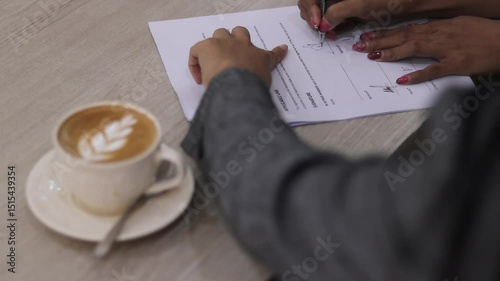 A person signing papers during meeting with cappuccino at hand. Illustrates business decision making, contract acceptance, and successful agreement.