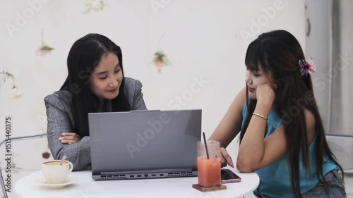 Two young women collaborating on a project at a cafe. They're using a laptop and having a discussion, creating a casual and collaborative environment.