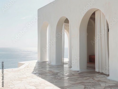 A white building with a balcony overlooking the ocean. The balcony has white curtains and a bench