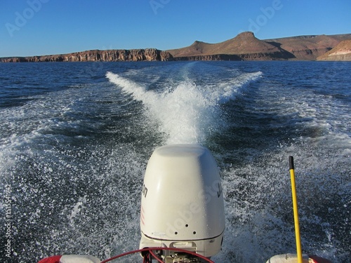 Rear view of a motorboat with splashes in the water moving away from Espiritu Santo Island