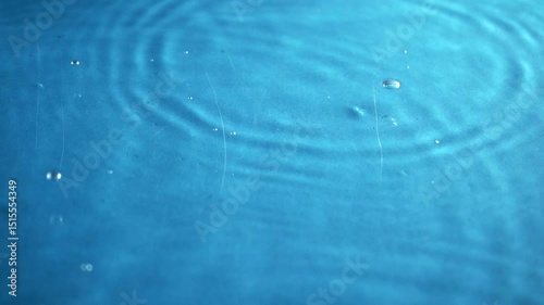 Blue water drops on a clear surface with gentle ripples and reflections