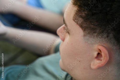 young man , teen boy with curly hair profile view, focused young man sitting outside, Close-up side portrait of teenager

