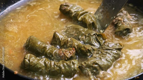 Homemade dolma with meat in grape leaves is stewed in a frying pan in meat broth. Medium shot.