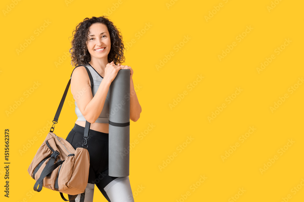 Fototapeta premium Mature woman with sports bag and fitness mat on yellow background