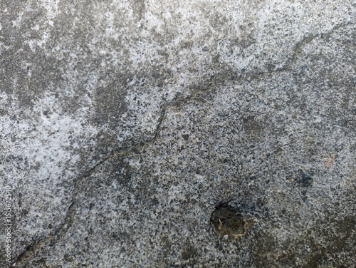Rough Stone Texture. A close-up view of a rugged stone surface with various shades of grey, granular details, and a visible crack