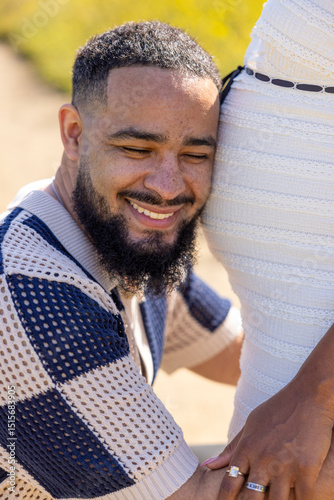 An African American couple joyfully embraces their pregnancy in a vibrant summer outdoor setting, reflecting their deep connection and excitement for the new arrival and future growth of their family