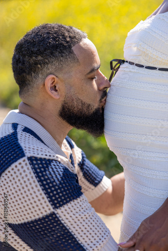 An African American couple joyfully celebrates their journey into parenthood, enjoying nature together. The wife, with her growing belly, relaxes peacefully in the warm summer sun